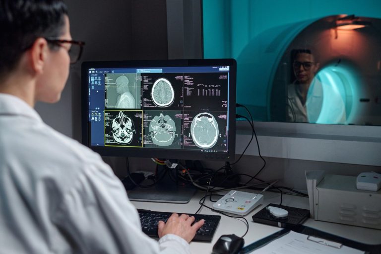Radiologist analyzes brain images from CT scan services Houston. Patient visible in scanner during diagnostic procedure.