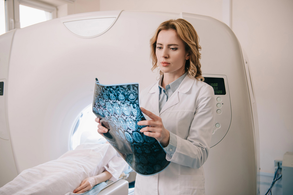 Female radiologist examining brain MRI scan films next to patient in scanner, providing expert analysis at premier MRI Houston clinic.