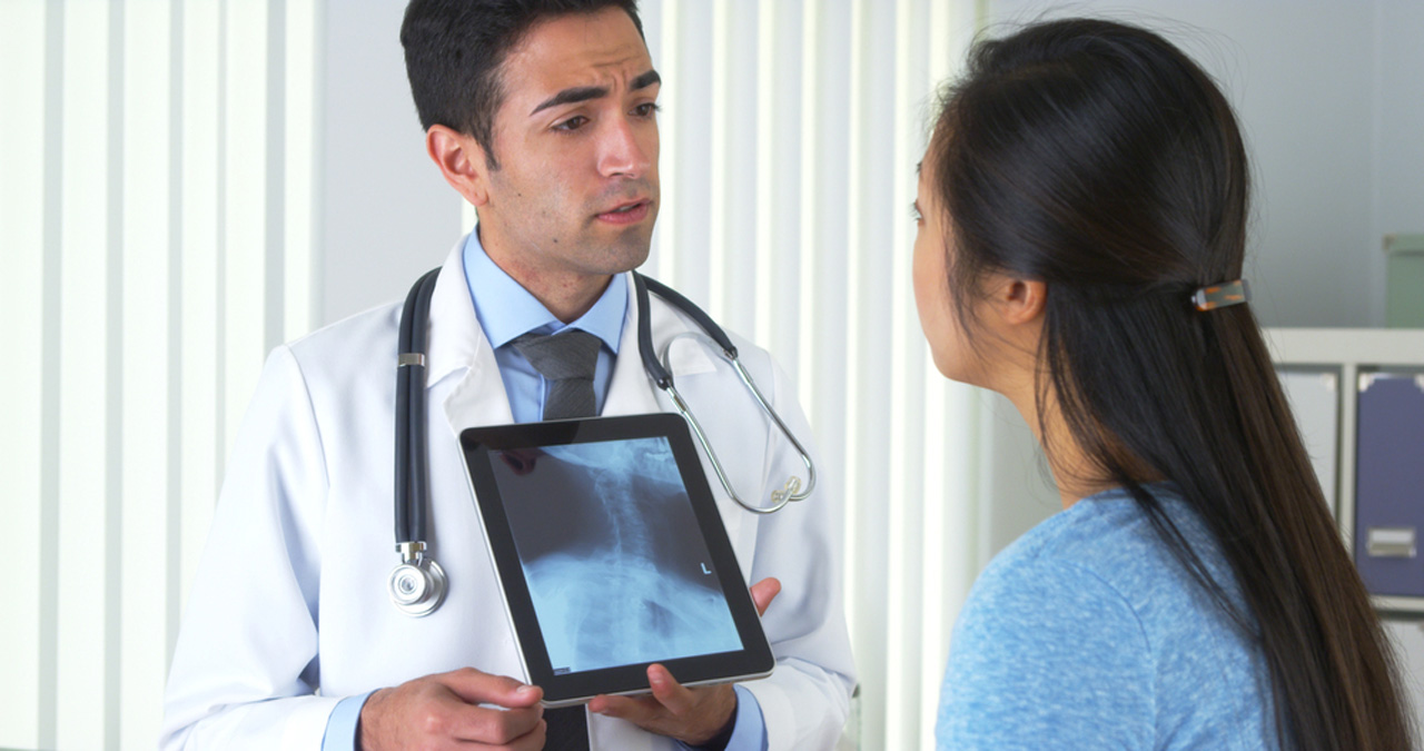 Male doctor showing chest X-ray results on tablet to patient during consultation at convenient walk-in X-ray center in Houston.