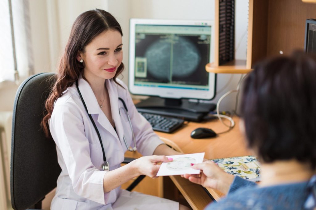 Houston doctor hands a patient a CD containing mammogram results, with breast x-rays visible on a computer monitor.
