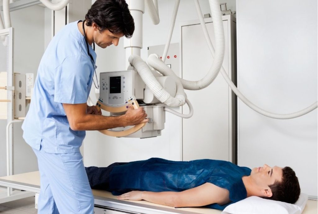 A male technician carefully positions a modern X-ray machine over a patient lying on a table for a walk in x ray houston.