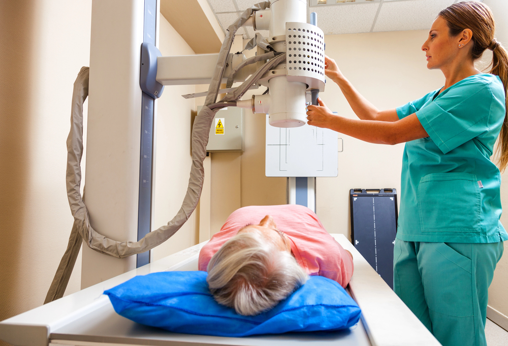 A medical technician in Houston operates a large x-ray machine over a patient lying on an examination table.