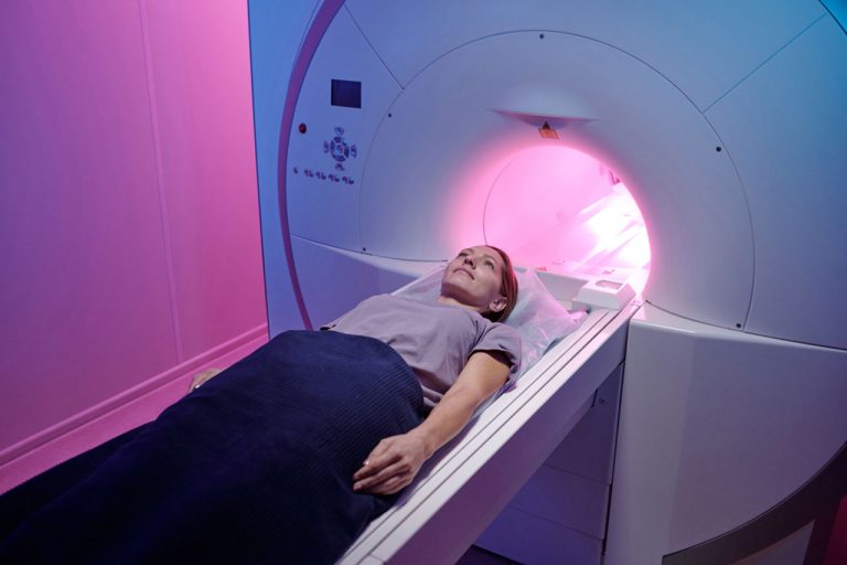 A woman patient smiles while lying down on the table of a modern MRI Houston machine for a diagnostic scan.