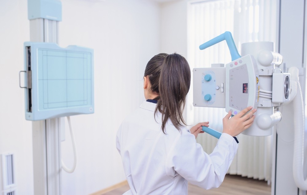 A doctor in a white coat operates the controls of a modern X-ray machine. This room is dedicated to advanced imaging. Comprehensive x-ray services houston.