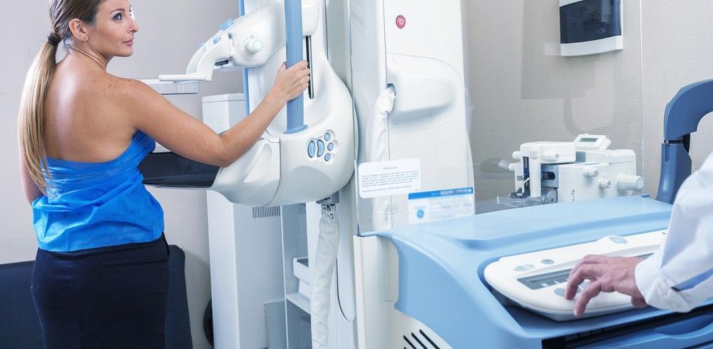 A side view of a blonde woman standing at a medical imaging device to receive professional mammogram services Houston.