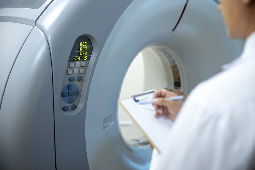 Doctor with clipboard reviewing data next to a medical scanner console, supporting access to mri scans houston.