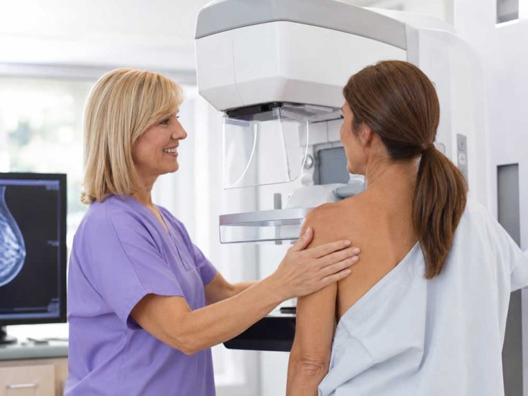A healthcare worker smiles at a patient by a screening machine for cheap mammograms in Houston.