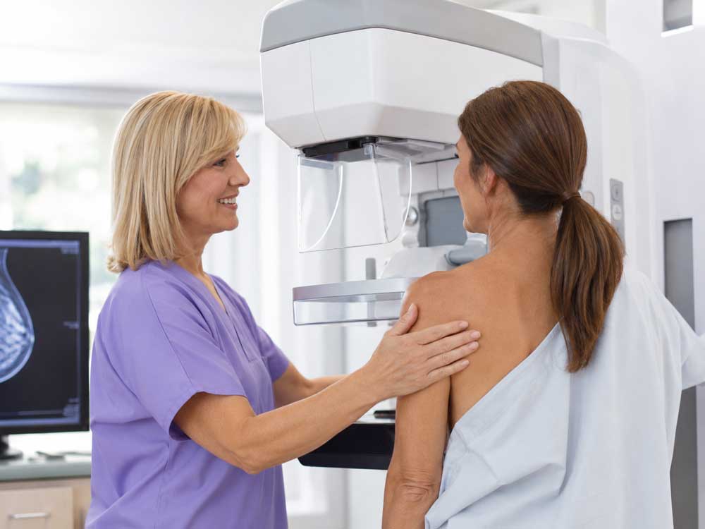 A healthcare worker smiles at a patient by a screening machine for cheap mammograms in Houston.